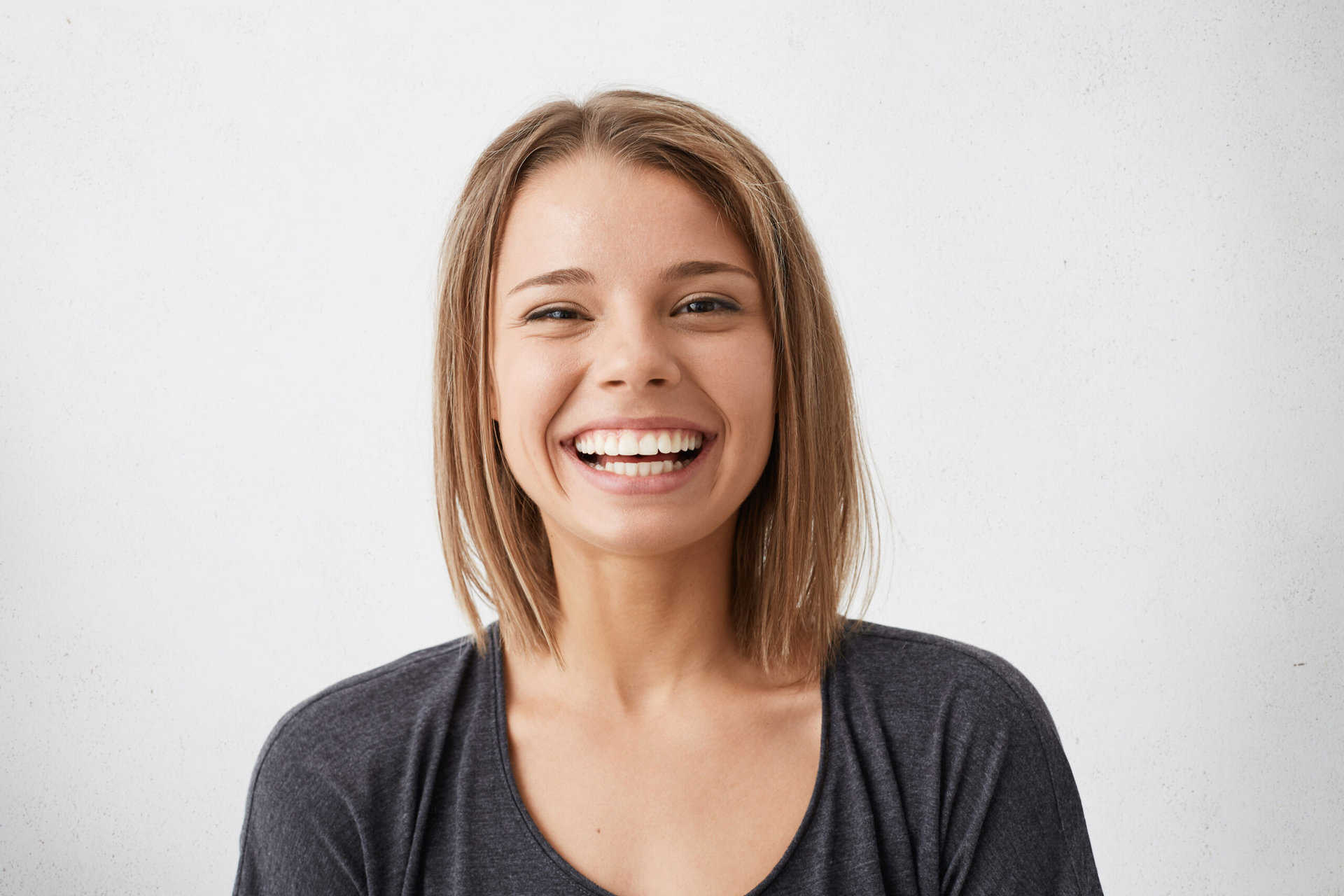 Positive human facial expressions and emotions. Cheerful attractive teenage girl with bob hairstyle grinning broadly, showing her perfect white teeth at camera while spending nice time indoors